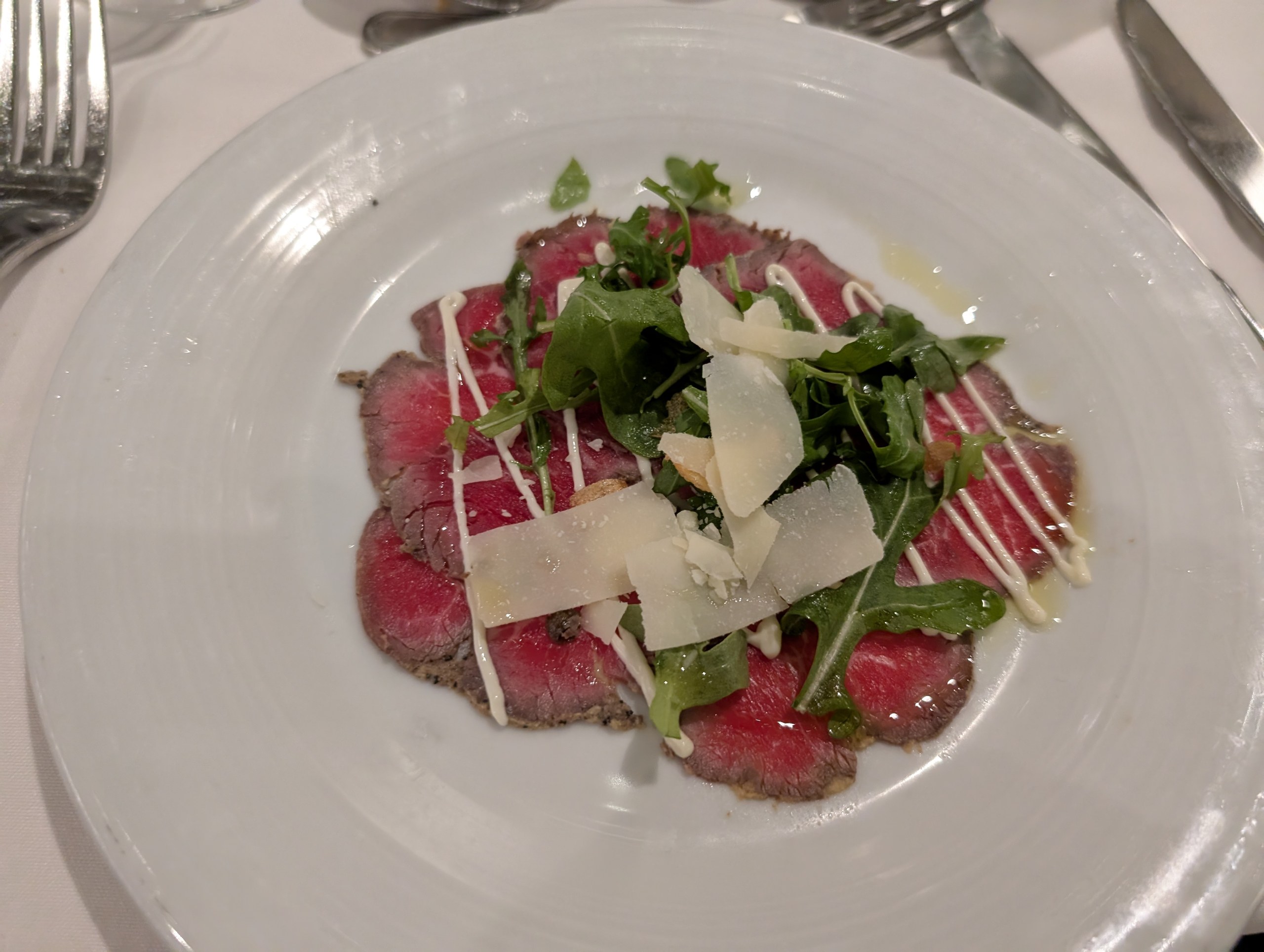 Plate of beef carpaccio with arugula, shaved parmesan, and crema at 150 Central Park, the specialty restaurant on Harmony of the Seas.