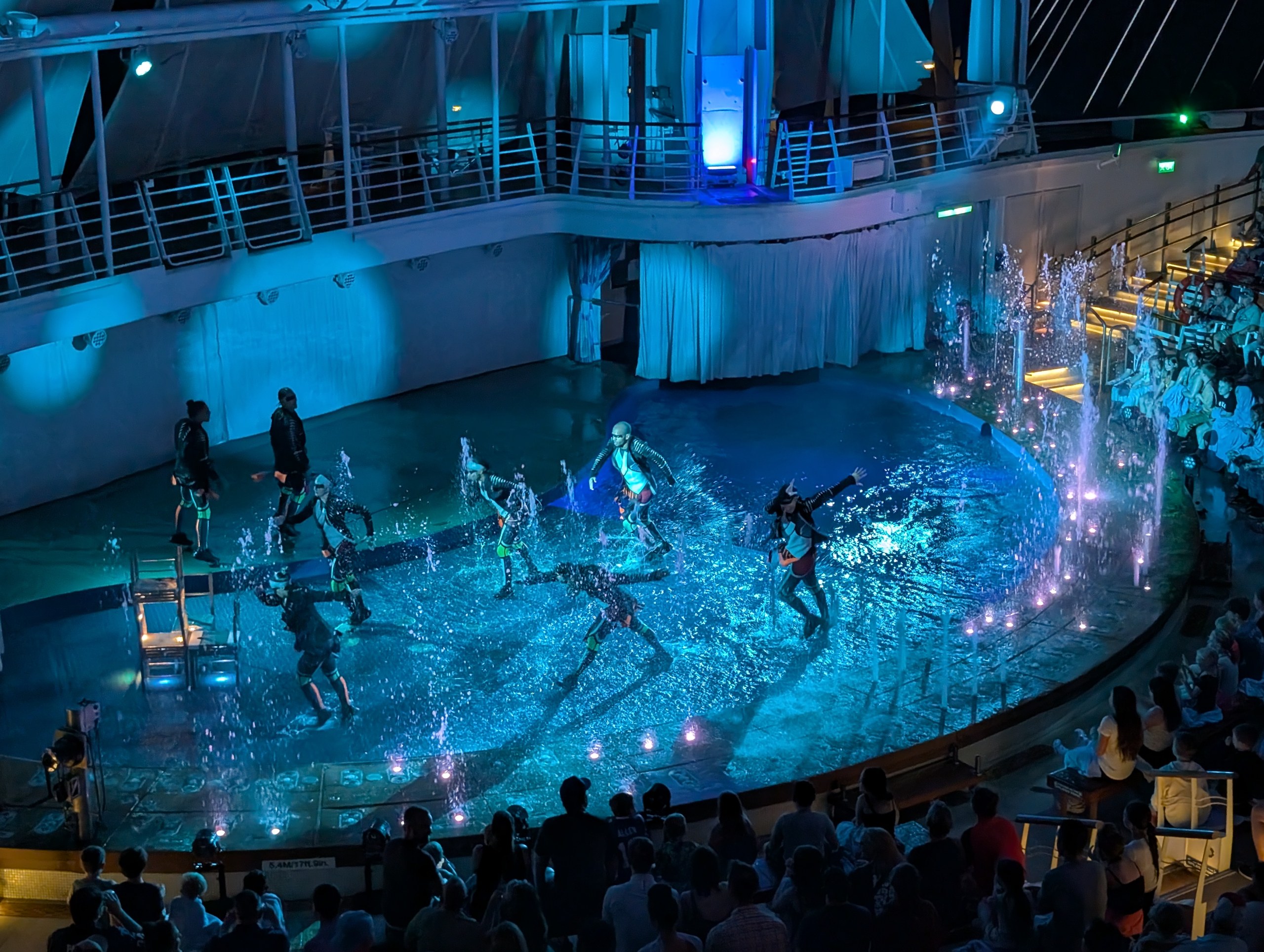 Performers in costumes diving into the AquaTheater pool with stage lighting and water jets at the back of Harmony of the Seas.