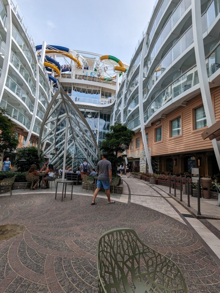 View from the Boardwalk neighborhood on Symphony of the Seas looking up at the Perfect Storm waterslides and the AquaTheater architecture, with the central glass elevator atrium below.