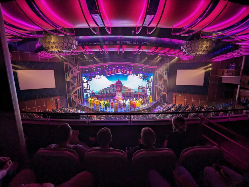 View from the balcony of the Royal Theater on Symphony of the Seas during a performance of Hairspray, with the cast lined up onstage in costume during the finale.