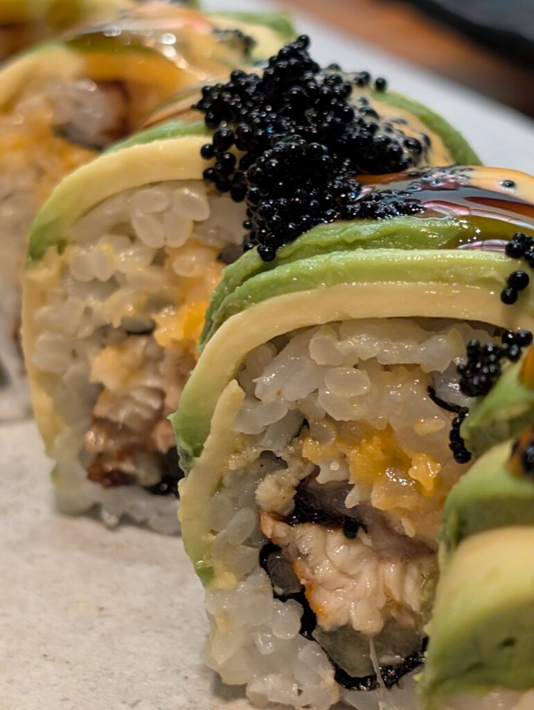 Macro close up of a single piece of the Black Dragon roll showing avocado layers and black tobiko