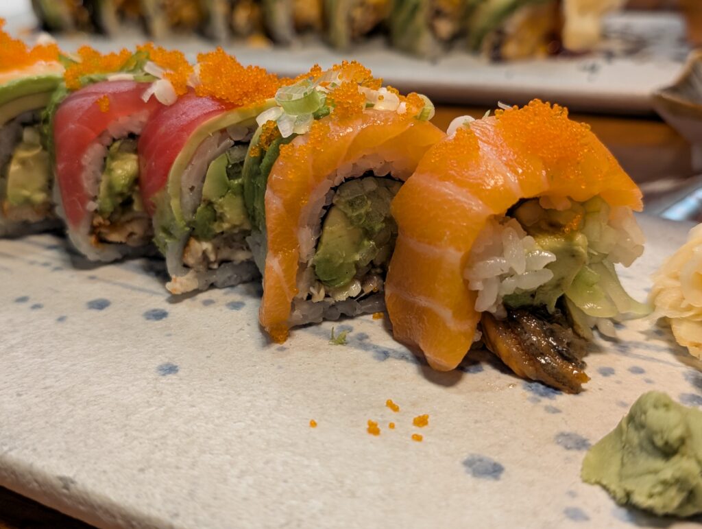 Close up of the Yuzu Tuna roll at Tekka Sushi, topped with tuna, salmon, avocado, and orange tobiko