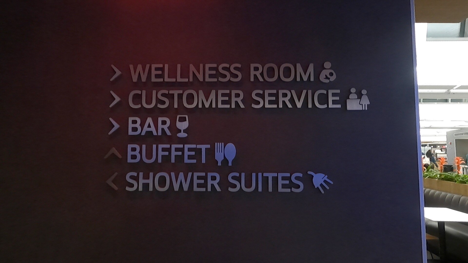 Amenities wayfinding sign at the United Club Newark pointing to wellness room, customer service, bar, buffet, and shower suites