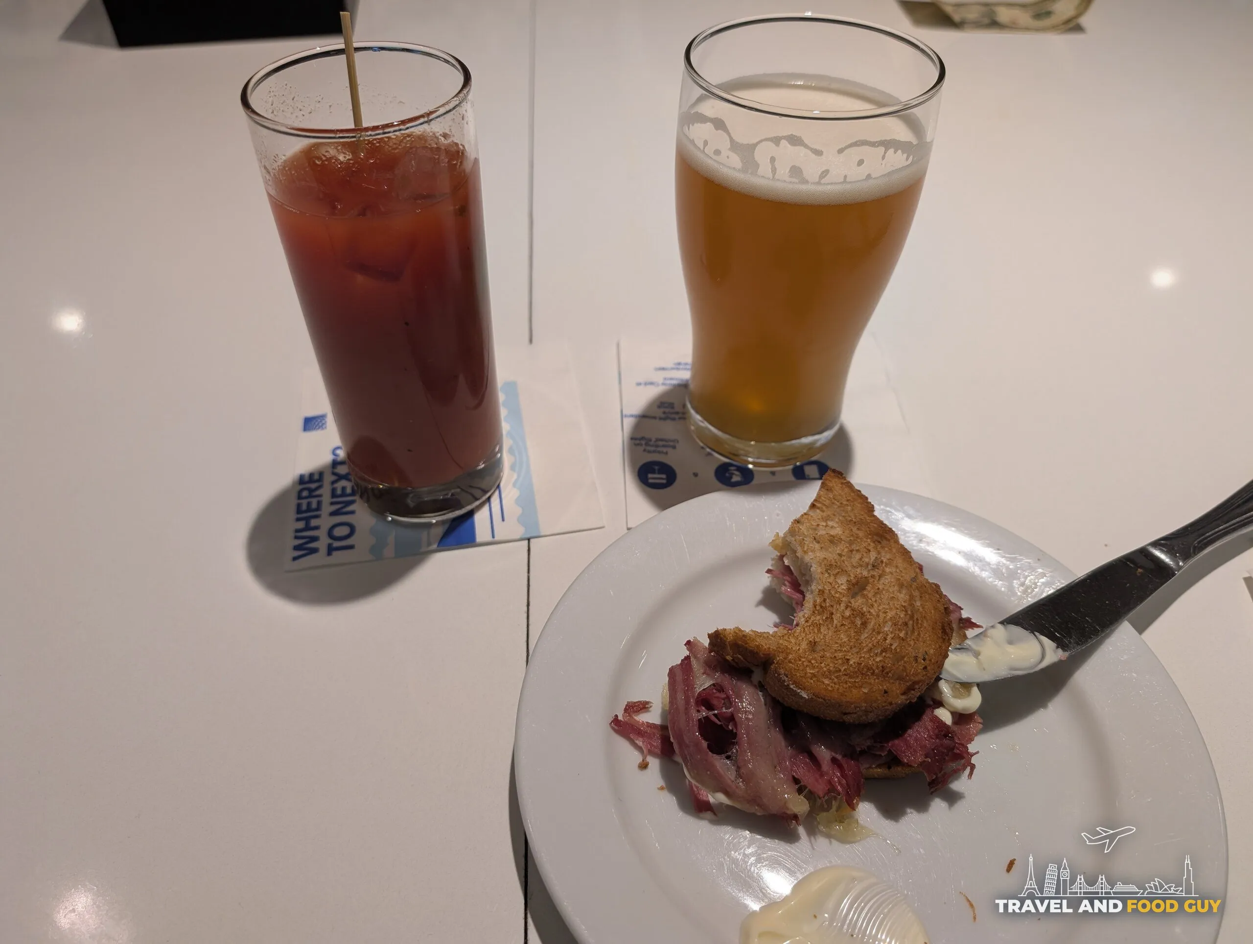 A hot roast beef sandwich on rye next to a bloody mary and a wheat beer at the United Club Newark Terminal C