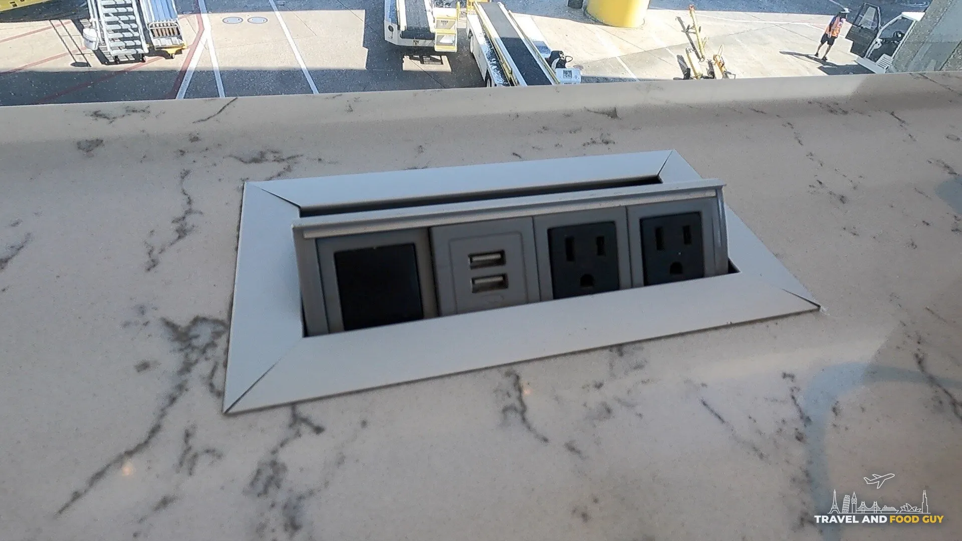Pop-up power station with two AC outlets and dual USB ports built into a marble window counter at the United Club Newark Terminal C