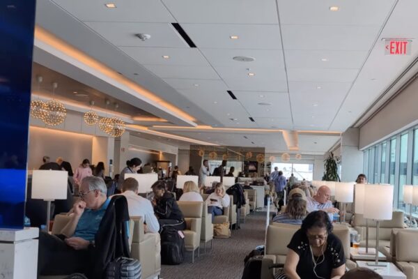 Wide view of the United Club by Gate C1 at IAH main lounge, with travelers seated in cream lounge chairs, modern pendant lights along the bar in the distance, and large windows on the right.