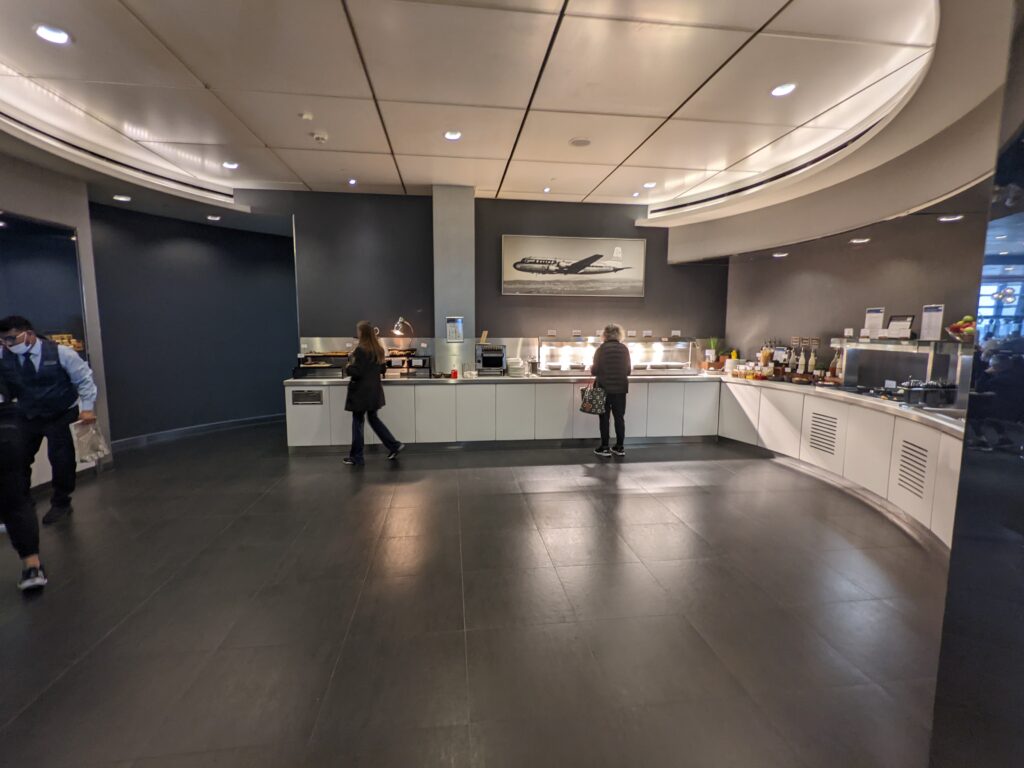 United Club LHR Terminal 2 buffet station with curved ceiling and a framed vintage United Capital Airlines aircraft photo on the wall.