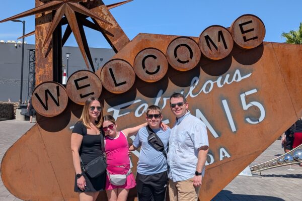 Alex, Vika, Josh and Emily posing at the rusted Welcome to Fabulous Area 15 parody sign outside the venue in Las Vegas