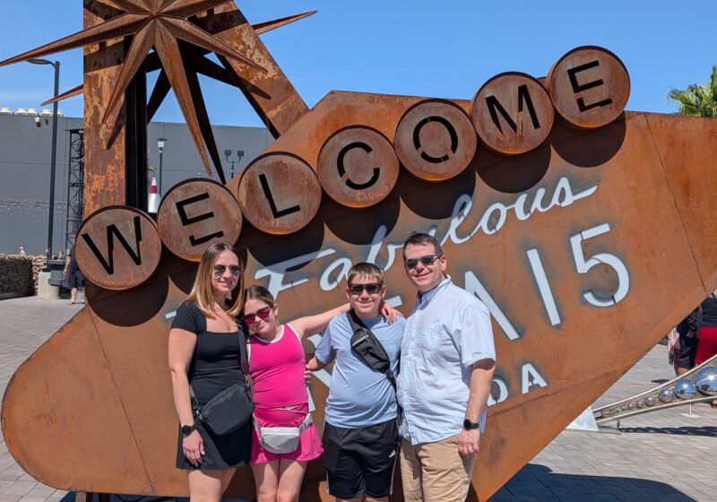 Alex, Vika, Josh and Emily posing at the rusted Welcome to Fabulous Area 15 parody sign outside the venue in Las Vegas