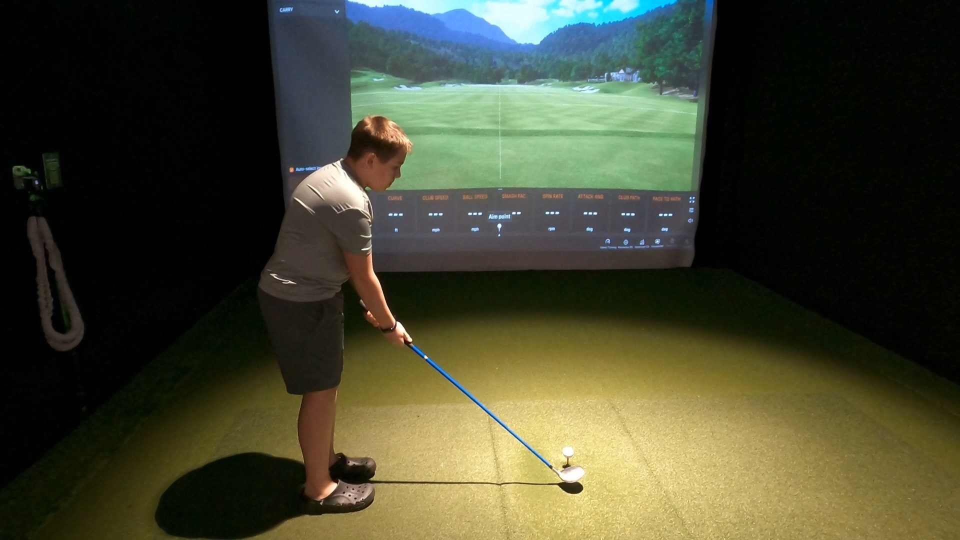 Josh setting up a tee shot inside the Five Iron Golf simulator booth at Area 15