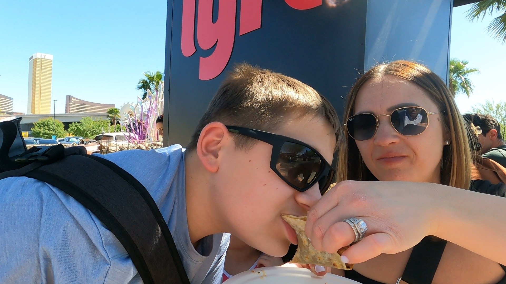 Josh eating a taco outside Area 15 with Vika feeding him a piece, the Wynn Las Vegas in the distance