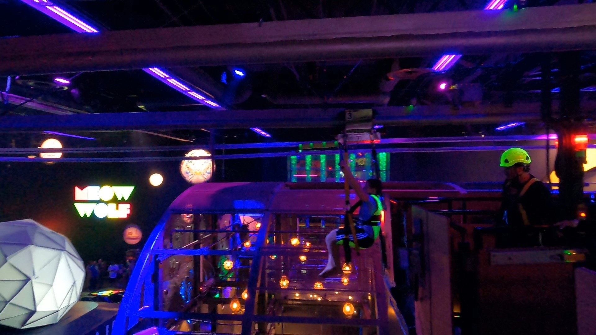 A rider zips overhead on the Halleys Comet zip line above the Area 15 concourse