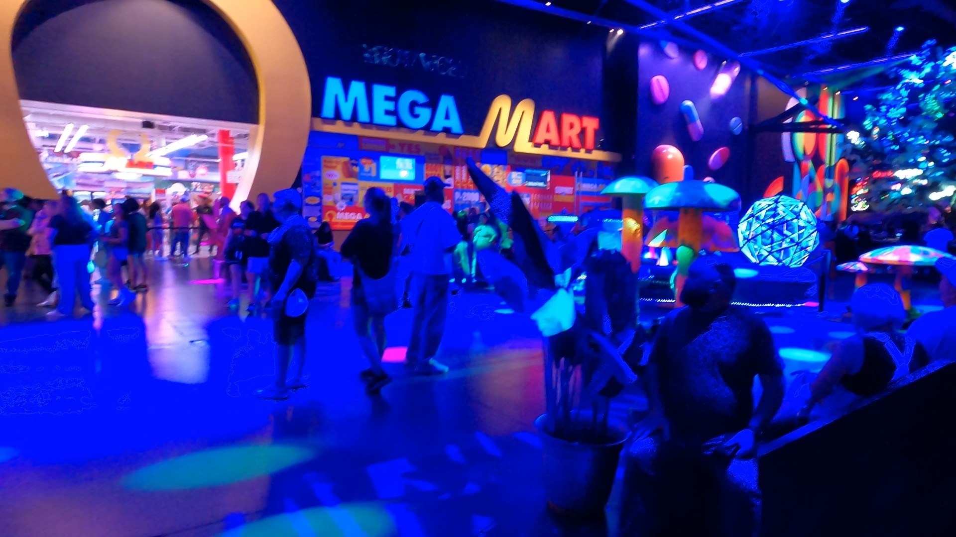 The Mega Mart neon entrance from the Area 15 concourse with crowds and immersive props