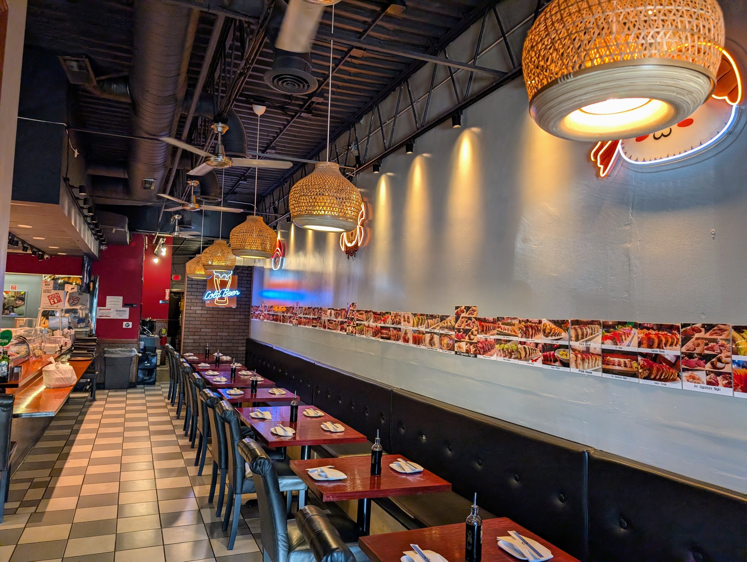 Ari Sushi dining room with red leather booths, woven pendant lights, checkered floor, and a wall of food photos