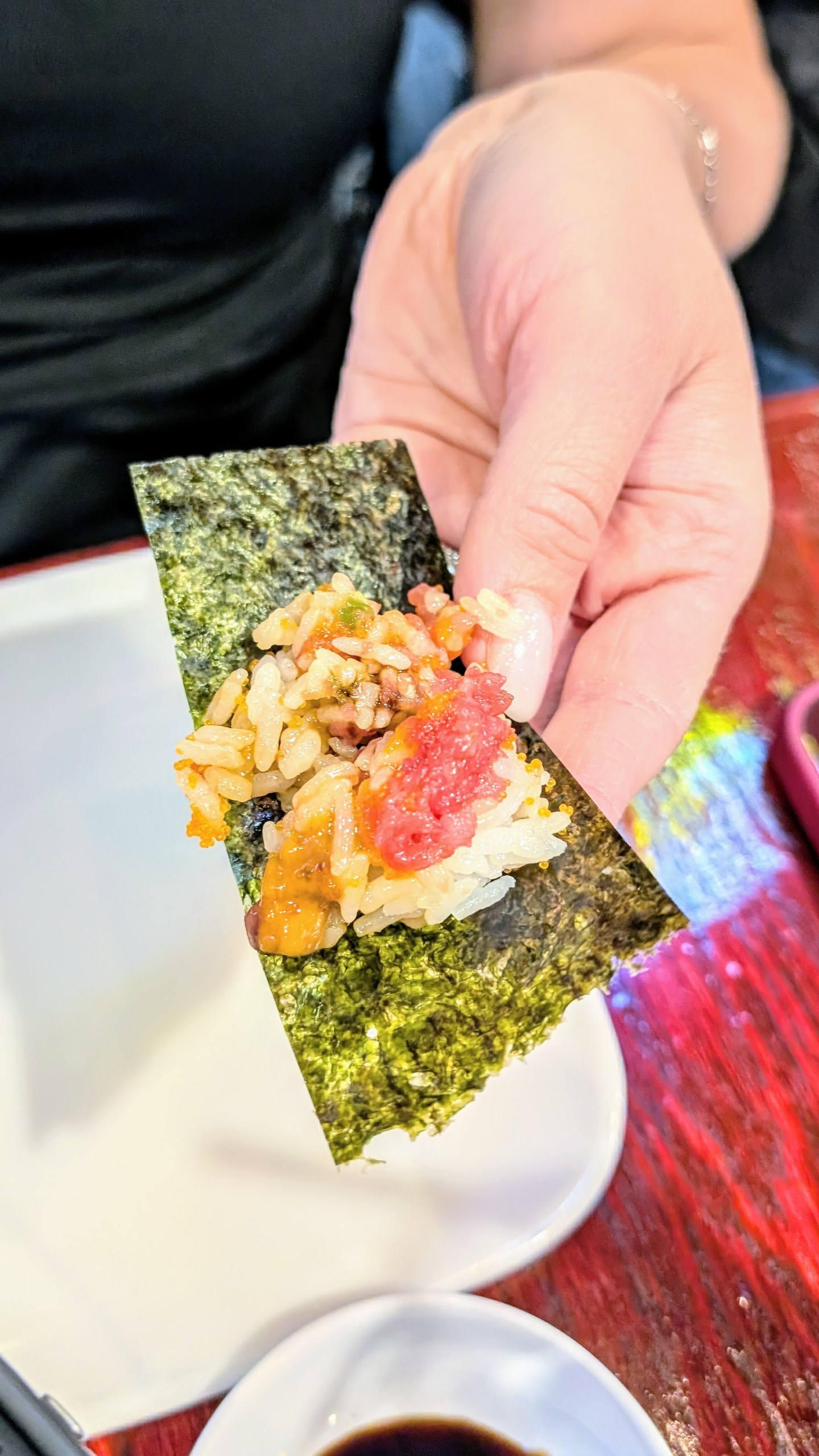 Hand holding a sheet of nori topped with mixed Unitoro Tartar, ready to eat like a hand roll