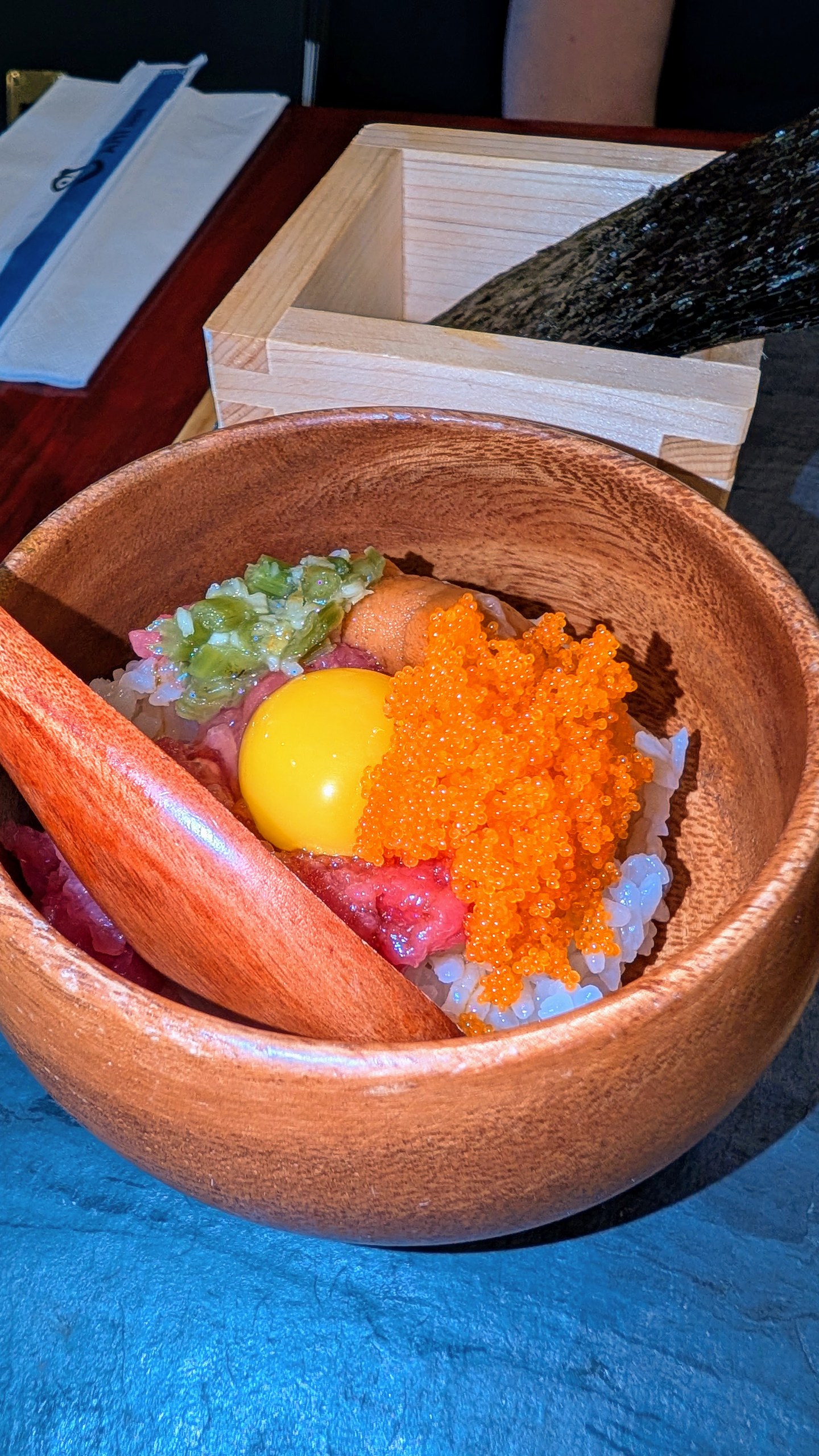 Unitoro Tartar appetizer in a wooden bowl, tuna and yellowtail tartar with a quail egg yolk and red tobiko, before mixing