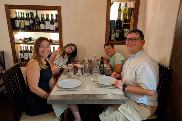 Family of four smiling at the table at Cantinetta delle Terme, Florence, candle lit and wine bottles backlit in the niche behind