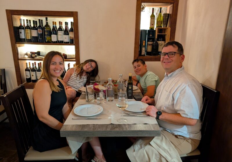 Family of four smiling at the table at Cantinetta delle Terme, Florence, candle lit and wine bottles backlit in the niche behind