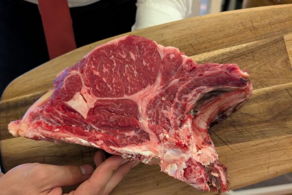 Server presents the raw bistecca alla Fiorentina T-bone on a wooden board at Da Aldone, Florence
