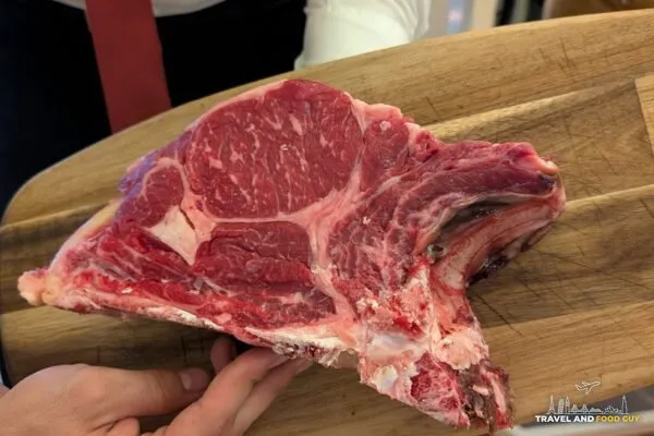 Server presents the raw bistecca alla Fiorentina T-bone on a wooden board at Da Aldone, Florence