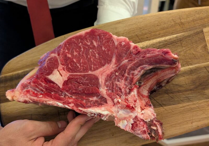 Server presents the raw bistecca alla Fiorentina T-bone on a wooden board at Da Aldone, Florence