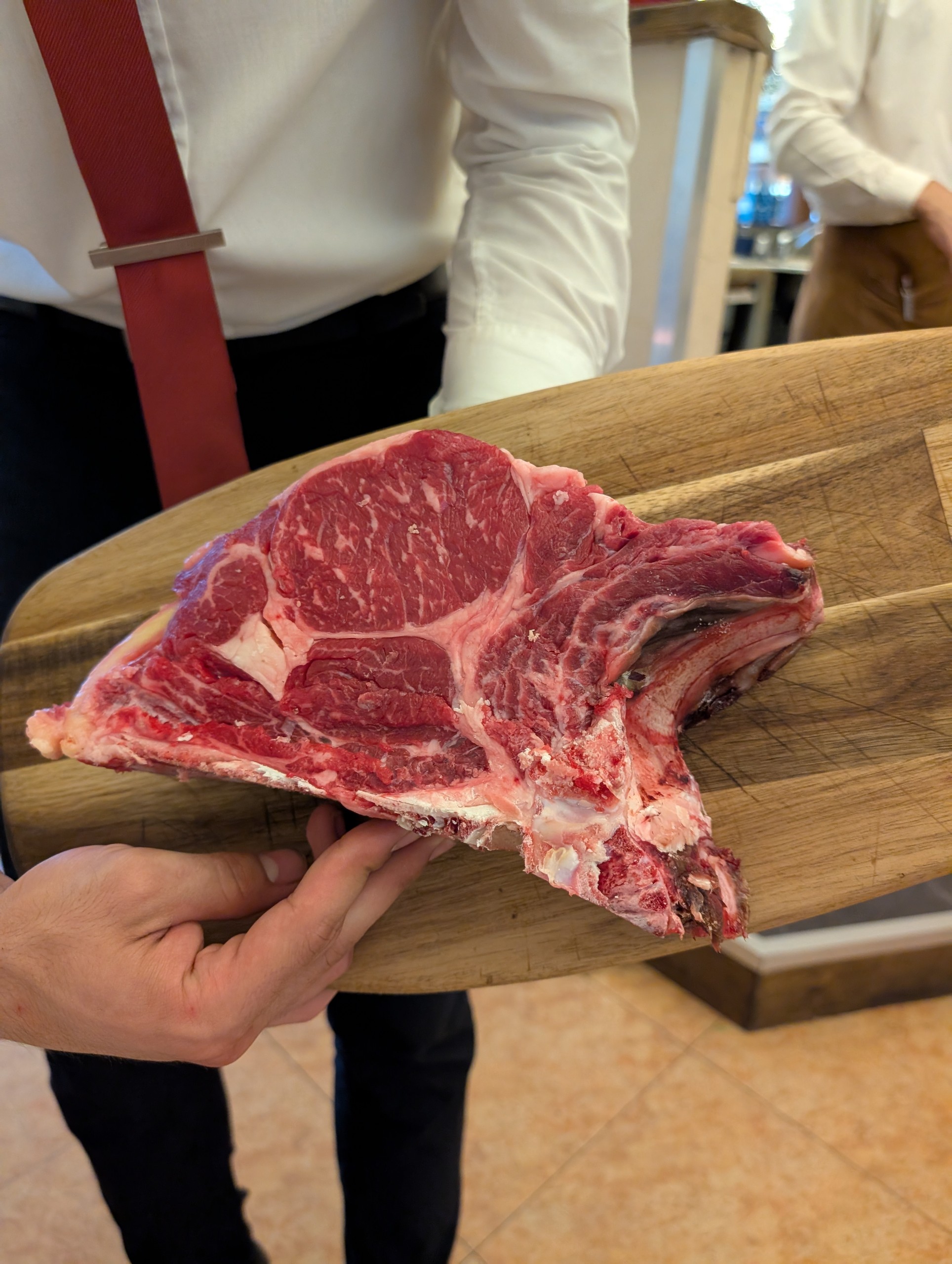 Server presents the raw bistecca alla Fiorentina T-bone on a wooden board at Da Aldone, Florence