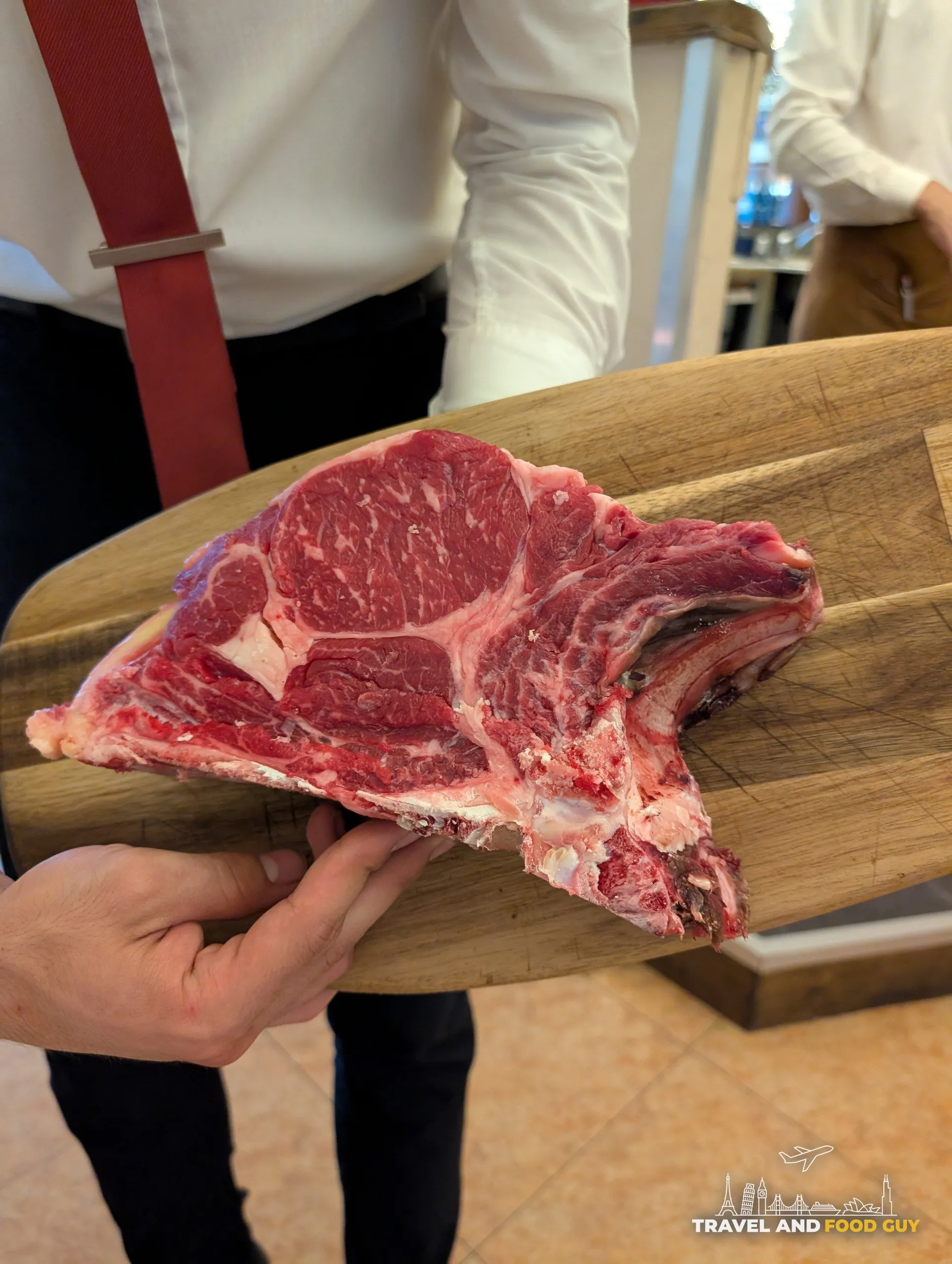 Server presents the raw bistecca alla Fiorentina T-bone on a wooden board at Da Aldone, Florence