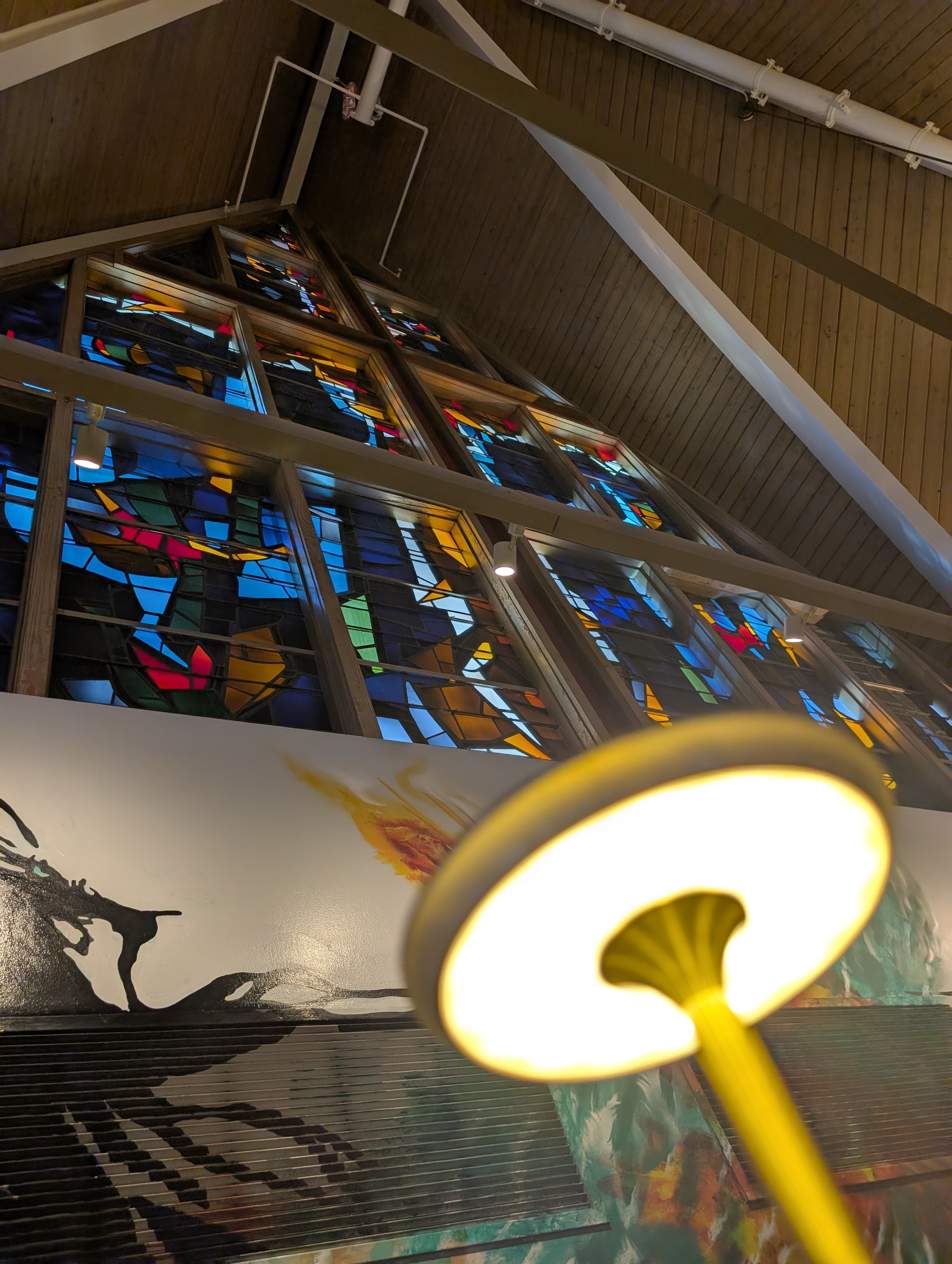 Mural and yellow lanterns under the stained glass at The Foxtail on the Lake