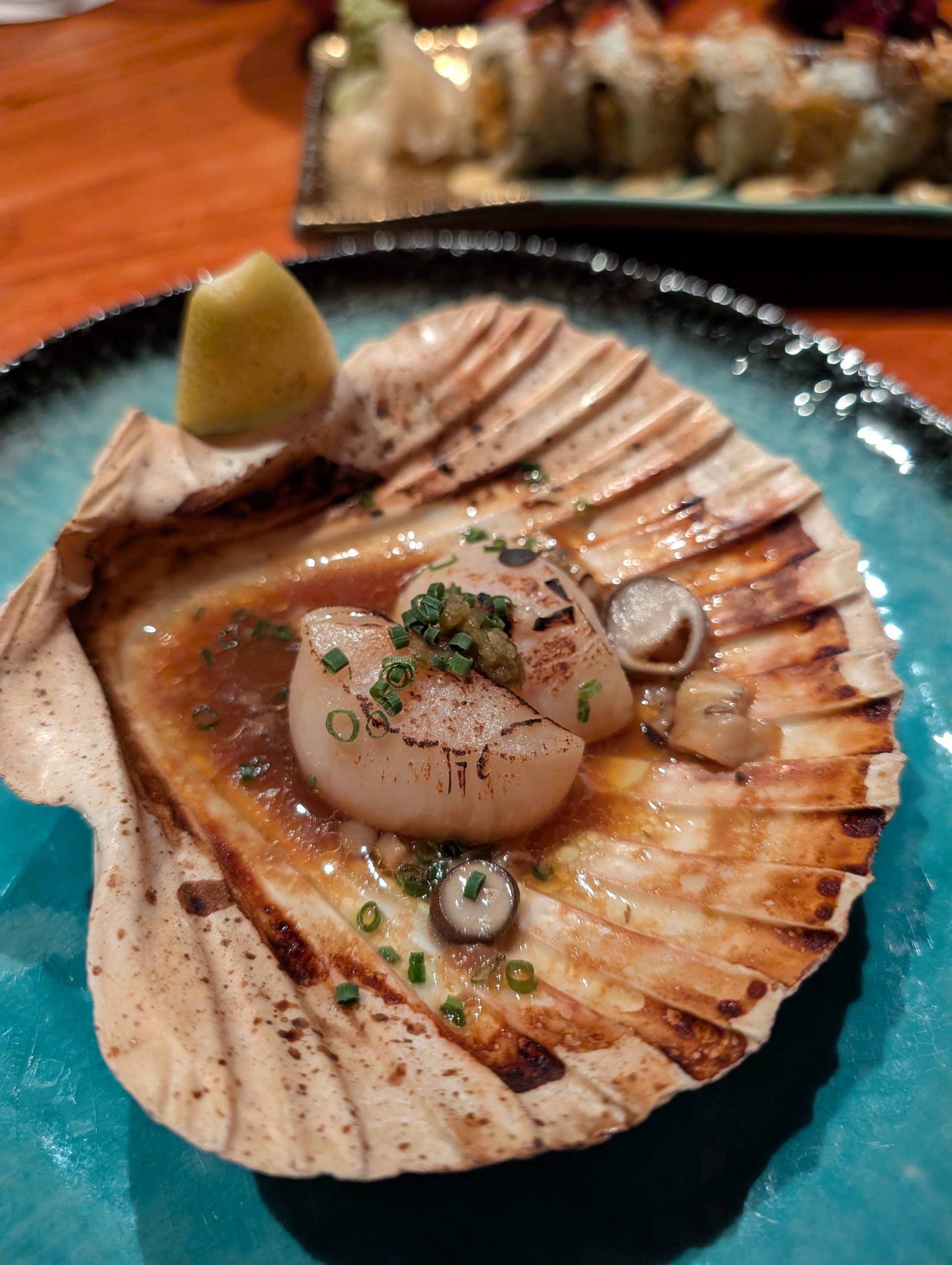 A grilled Hokkaido scallop served in its shell at KOMA Singapore, with butter soy, chives, and a yuzu wedge.