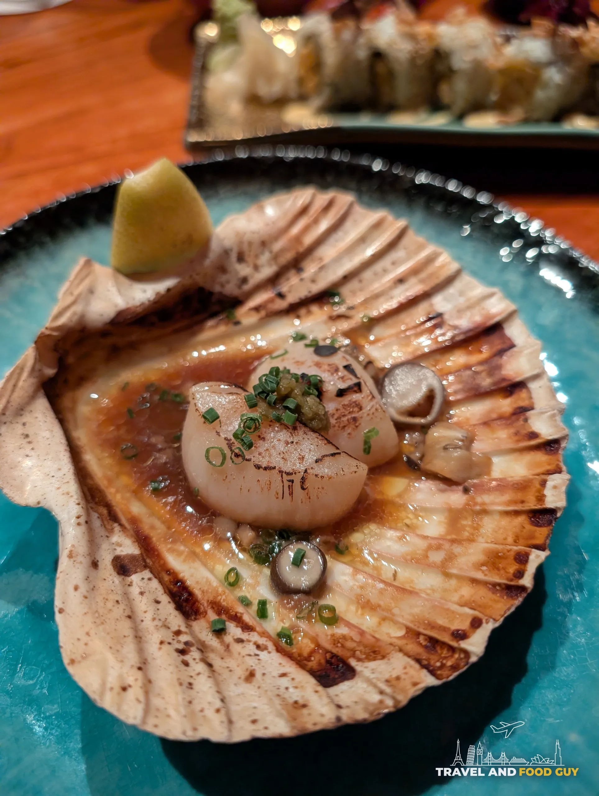 A grilled Hokkaido scallop served in its shell at KOMA Singapore, with butter soy, chives, and a yuzu wedge.