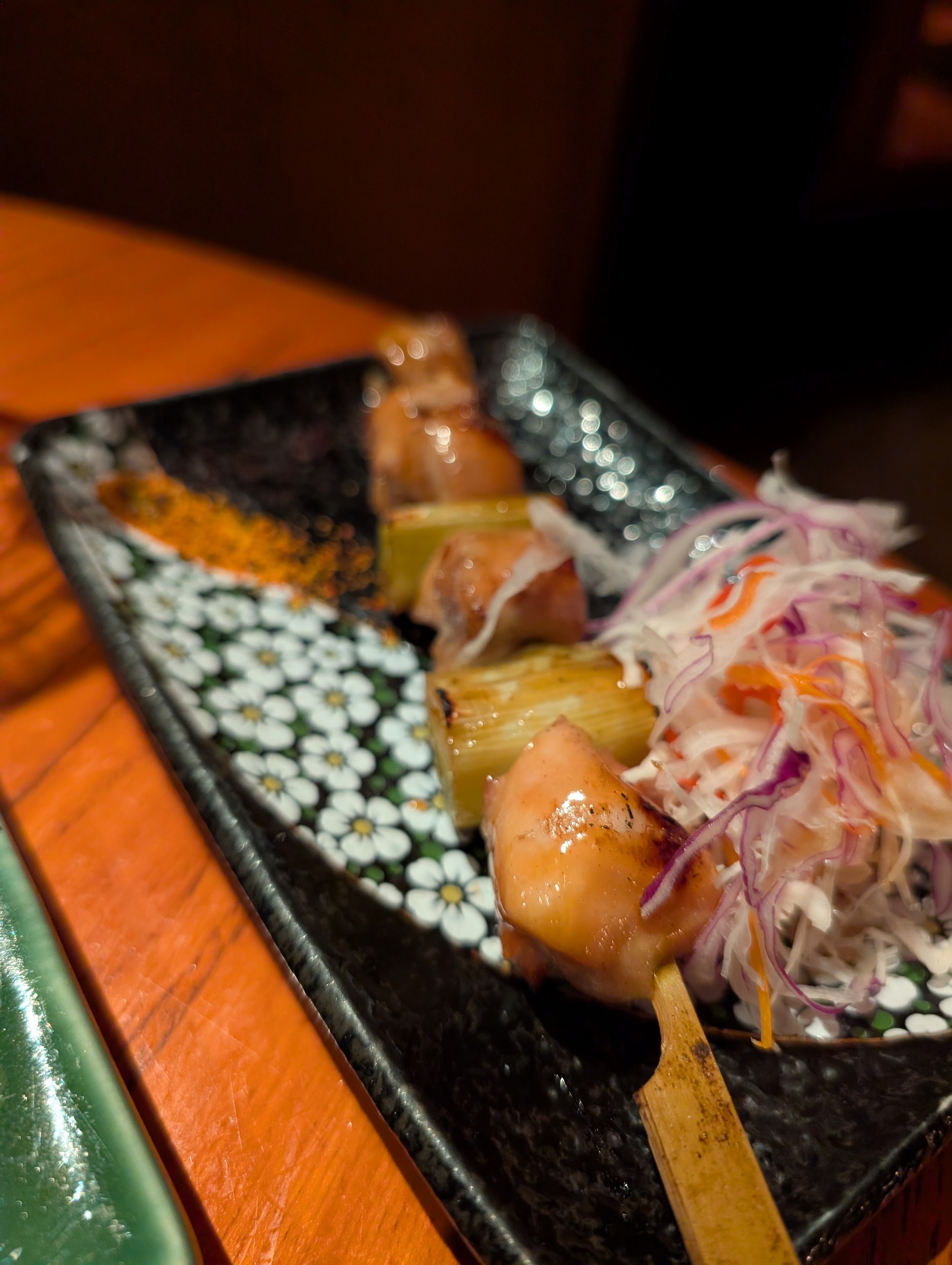 Two Negima yakitori skewers at KOMA Singapore, chicken thigh alternating with Tokyo negi, served with shaved cabbage and shichimi.