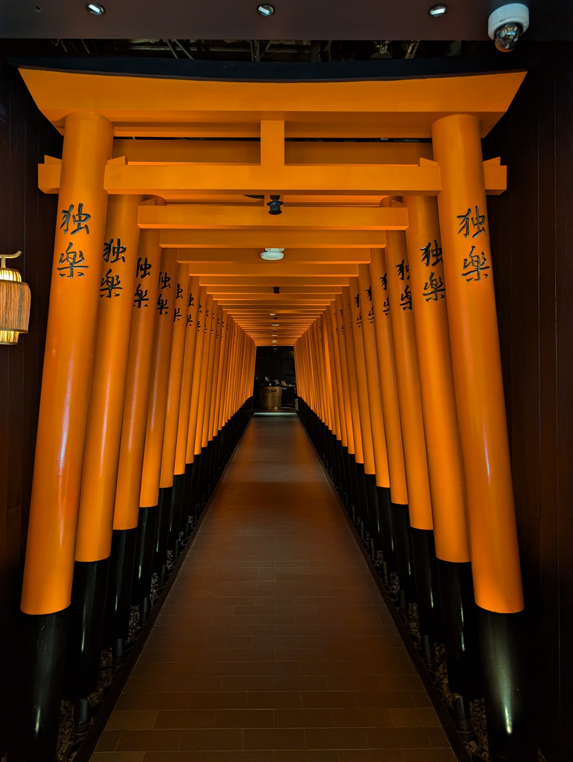 The orange torii gate hallway at the entrance of KOMA Singapore, with Japanese kanji characters across the crossbeams.