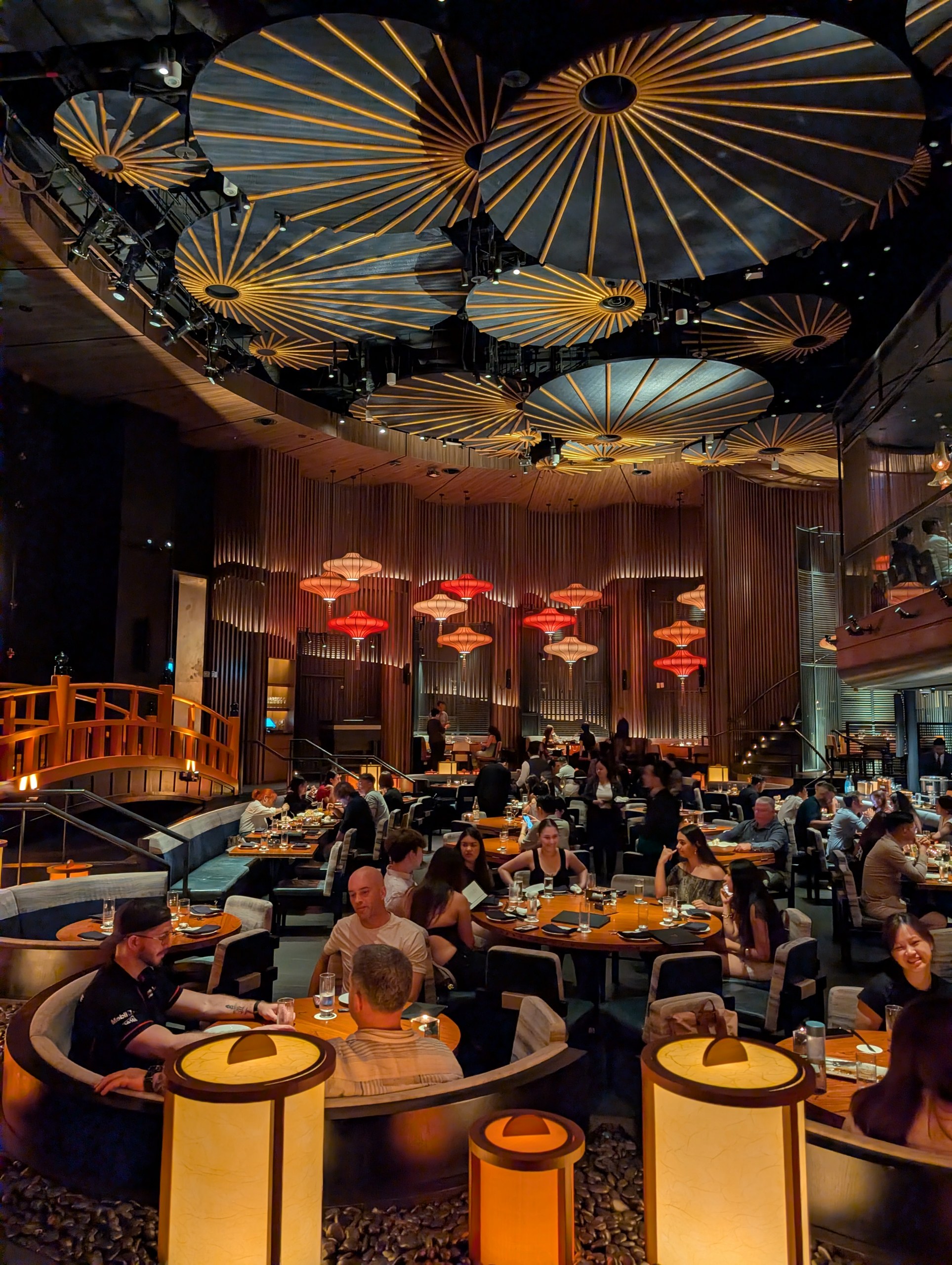 The wooden footbridge leading into the main dining room at KOMA Singapore, with the bronze bell visible in the background.