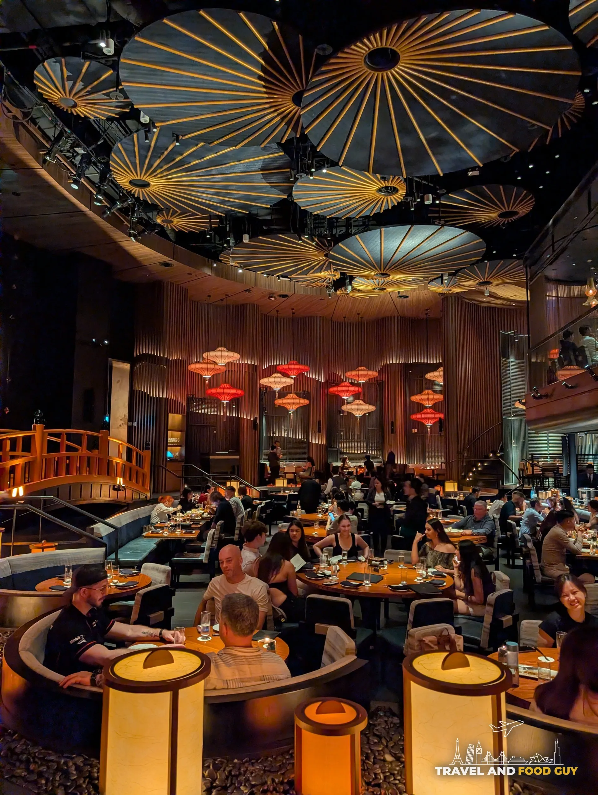 The wooden footbridge leading into the main dining room at KOMA Singapore, with the bronze bell visible in the background.