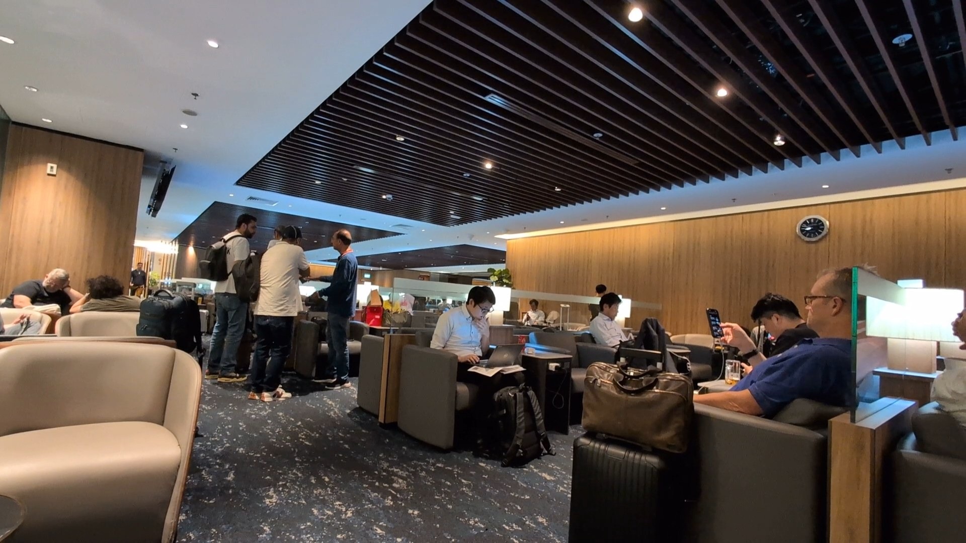 Busy evening crowd in the KrisFlyer Gold Lounge with travelers working on laptops and gathering at the buffet.