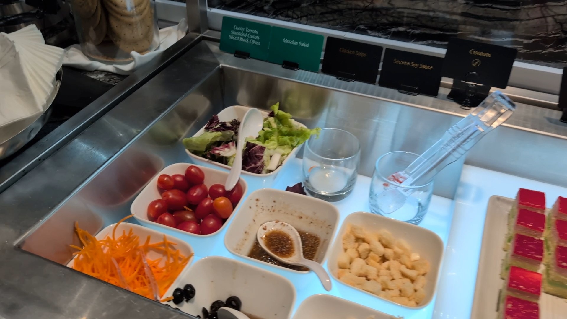 Salad bar with mesclun, cherry tomatoes, shredded carrots, croutons and dressings at the cold station.