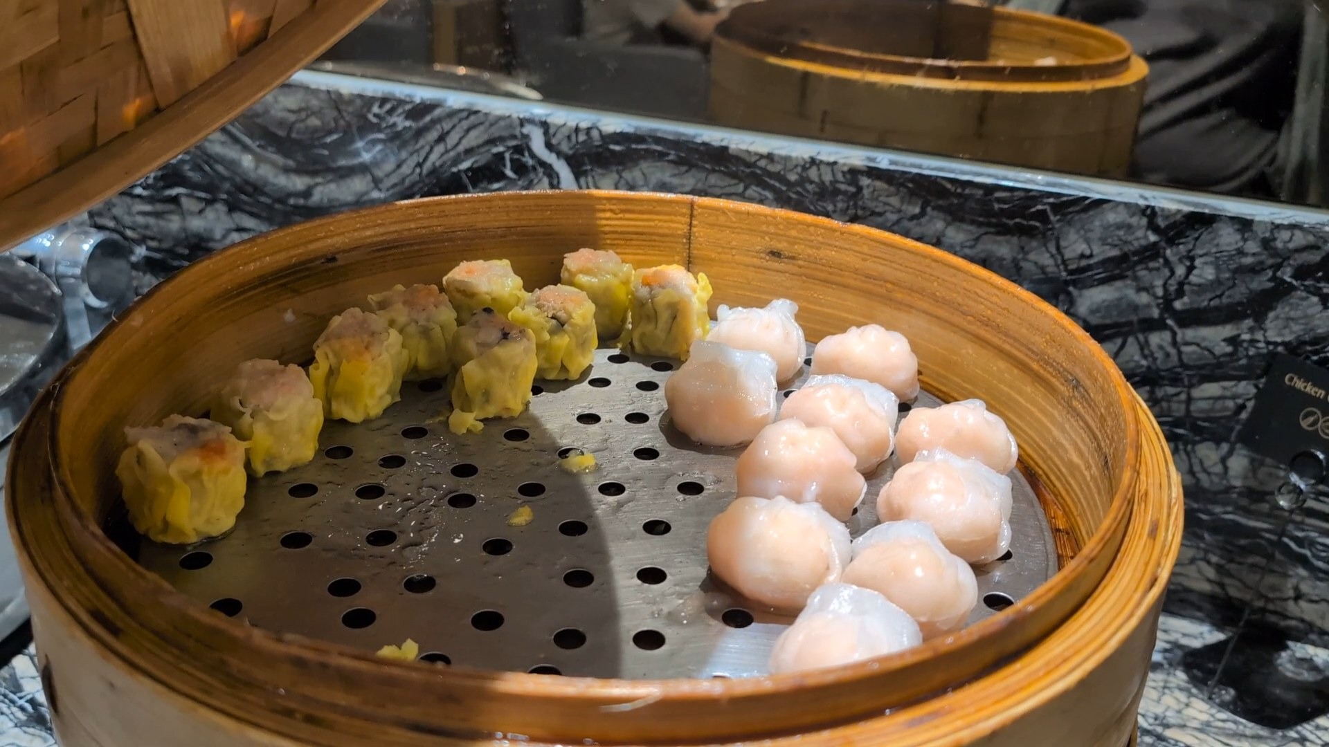 Shumai and har gow dumplings in a bamboo steamer at the KrisFlyer Gold Lounge dim sum line.