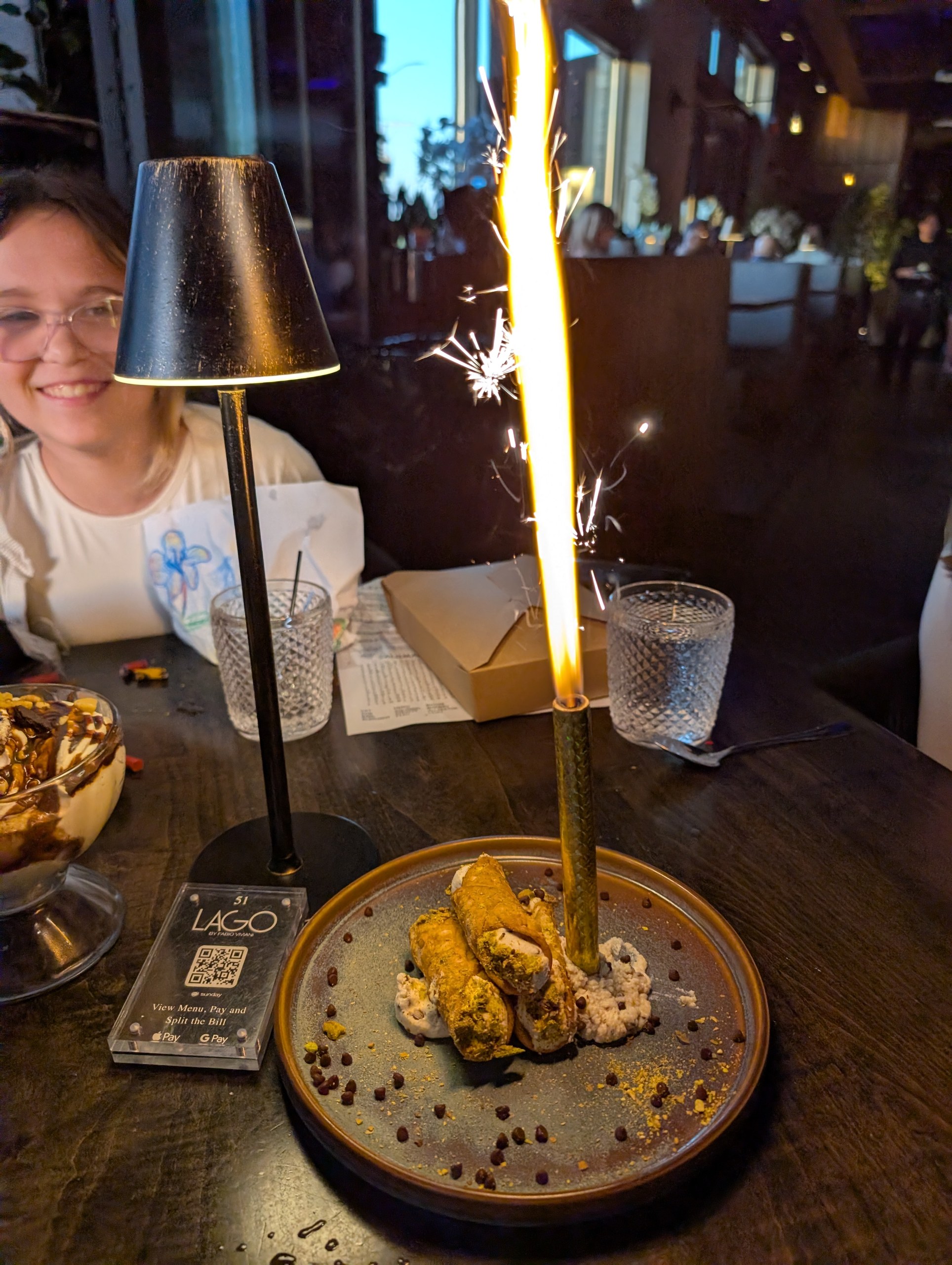 Cannoli with a giant sparkler arriving at the table for an early Mother's Day at LAGO Lake Zurich, Emily smiling in the background