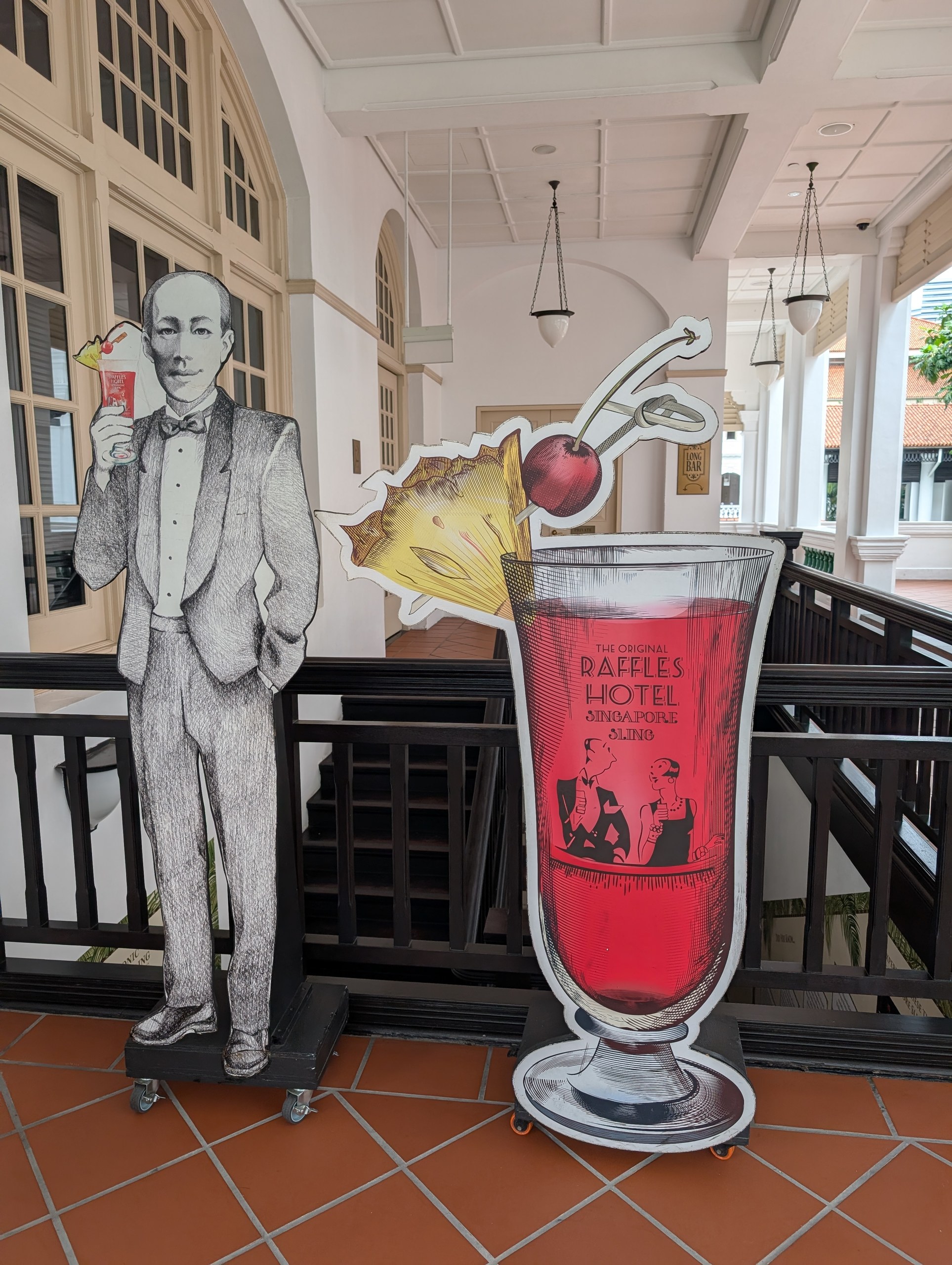 Life-size cutouts at the entrance of Long Bar, one of the original bartender holding a Singapore Sling and one of a giant Singapore Sling glass, set up as a photo op