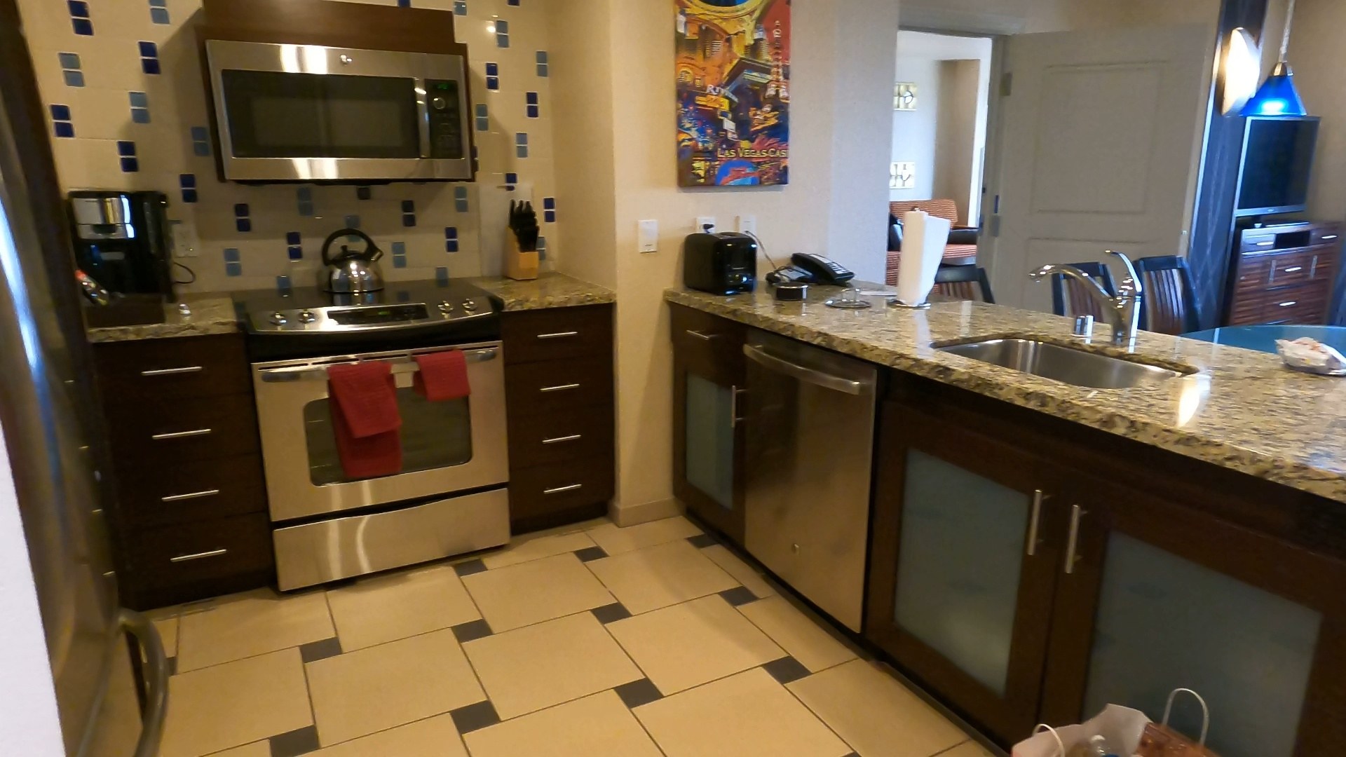 Wide view of the full kitchen in the Marriott Grand Chateau two-bedroom suite with stove, oven, microwave, dishwasher, granite counters and Las Vegas wall art