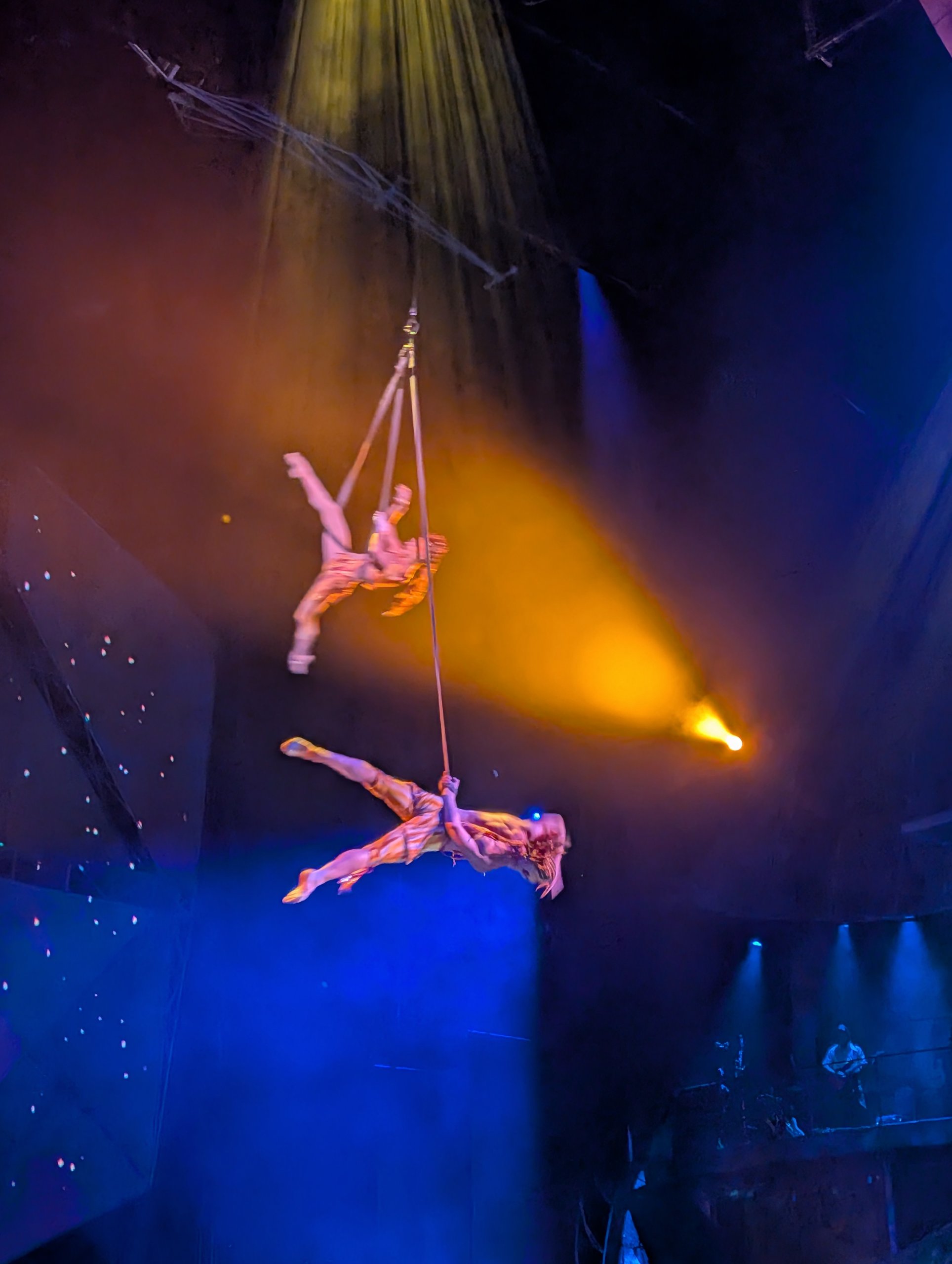 Two Mystère aerialists performing on straps high above the Treasure Island stage in yellow spotlight