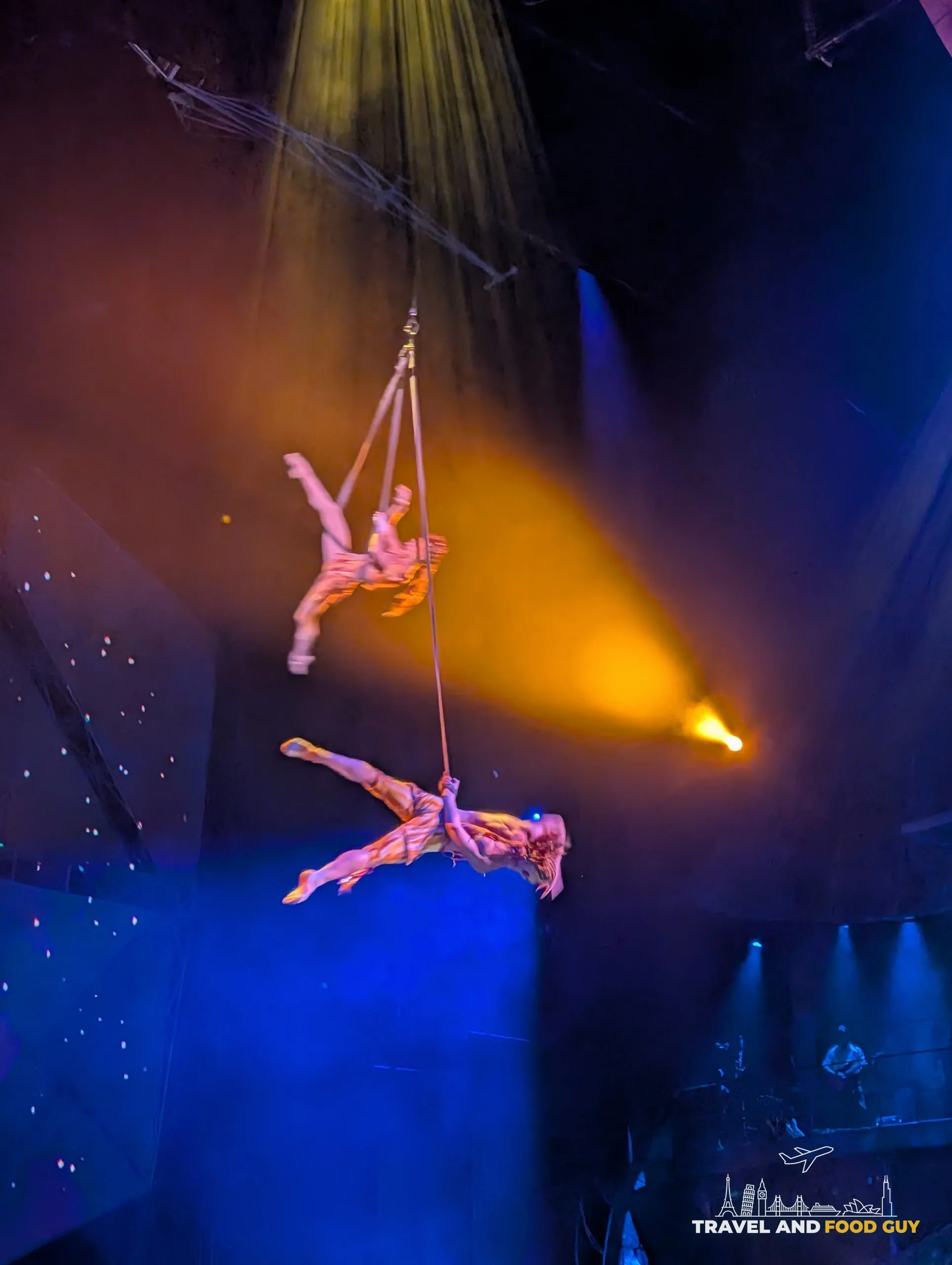 Two Mystère aerialists performing on straps high above the Treasure Island stage in yellow spotlight