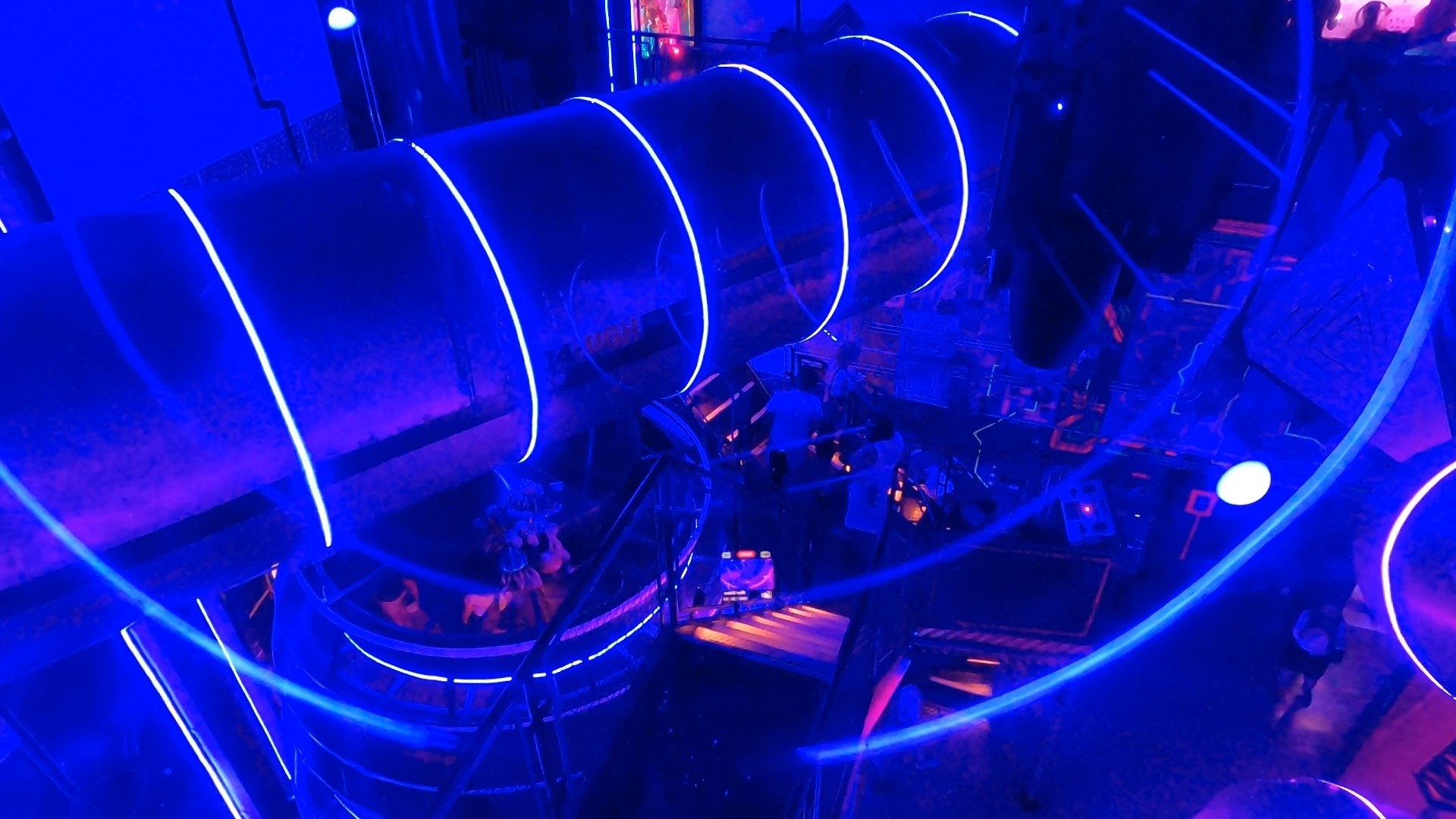 Blue neon spiral slide tube connecting two floors of the Omega Mart immersive experience