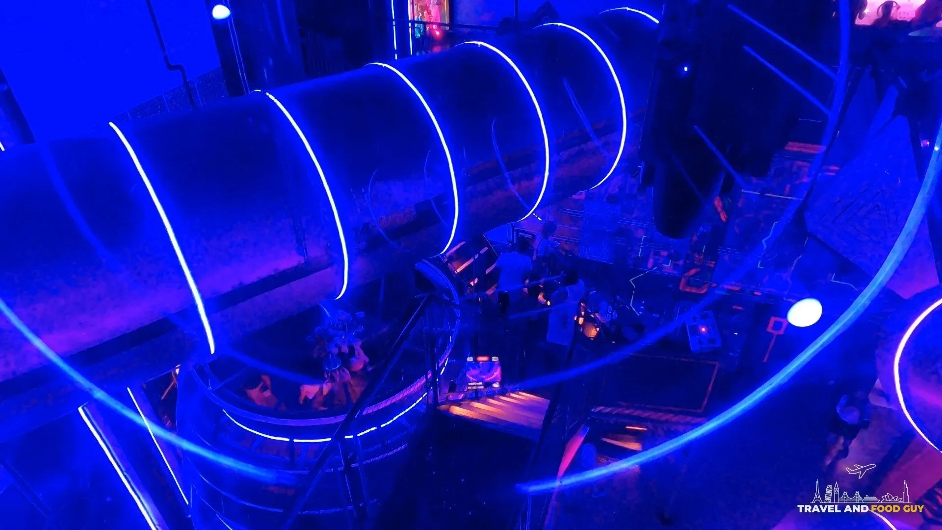 Blue neon spiral slide tube connecting two floors of the Omega Mart immersive experience