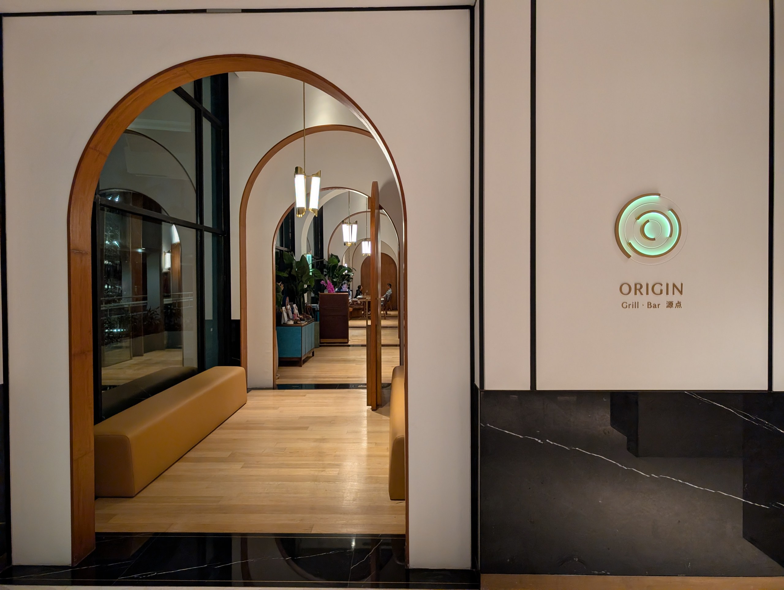 The timber arched entrance to Origin Grill and Bar at Shangri-La Singapore, with the Origin Grill Bar sign on the right wall.