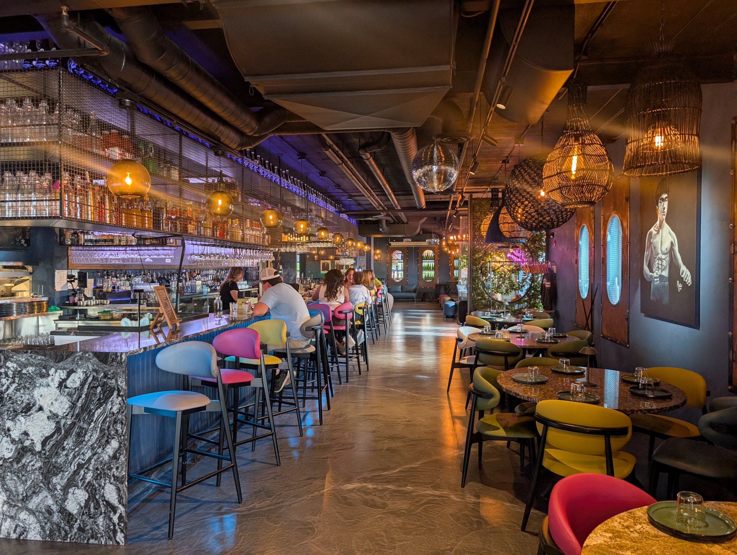 Long bar at Ostras Lounge with colorful stools, bottle-stocked archways, and pendant lighting