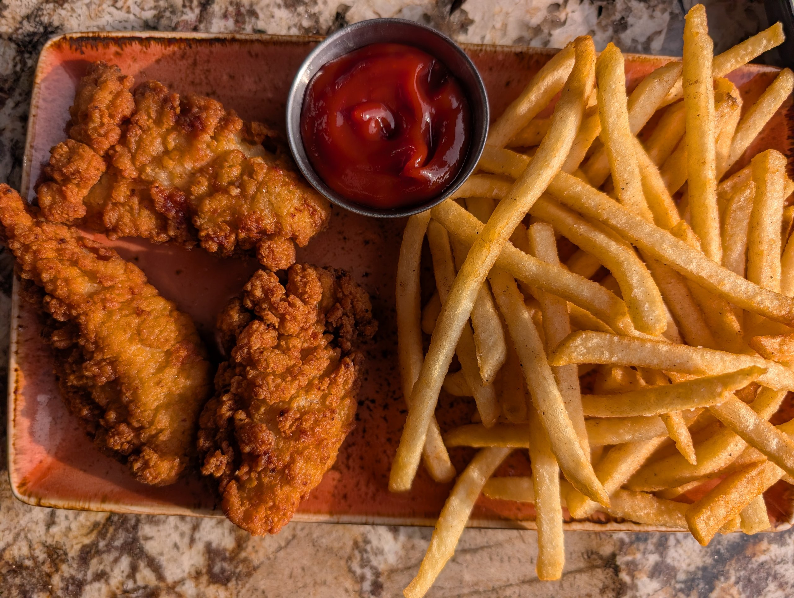 Plate of breaded chicken tenders and fries with a small cup of ketchup at Ostras Lounge