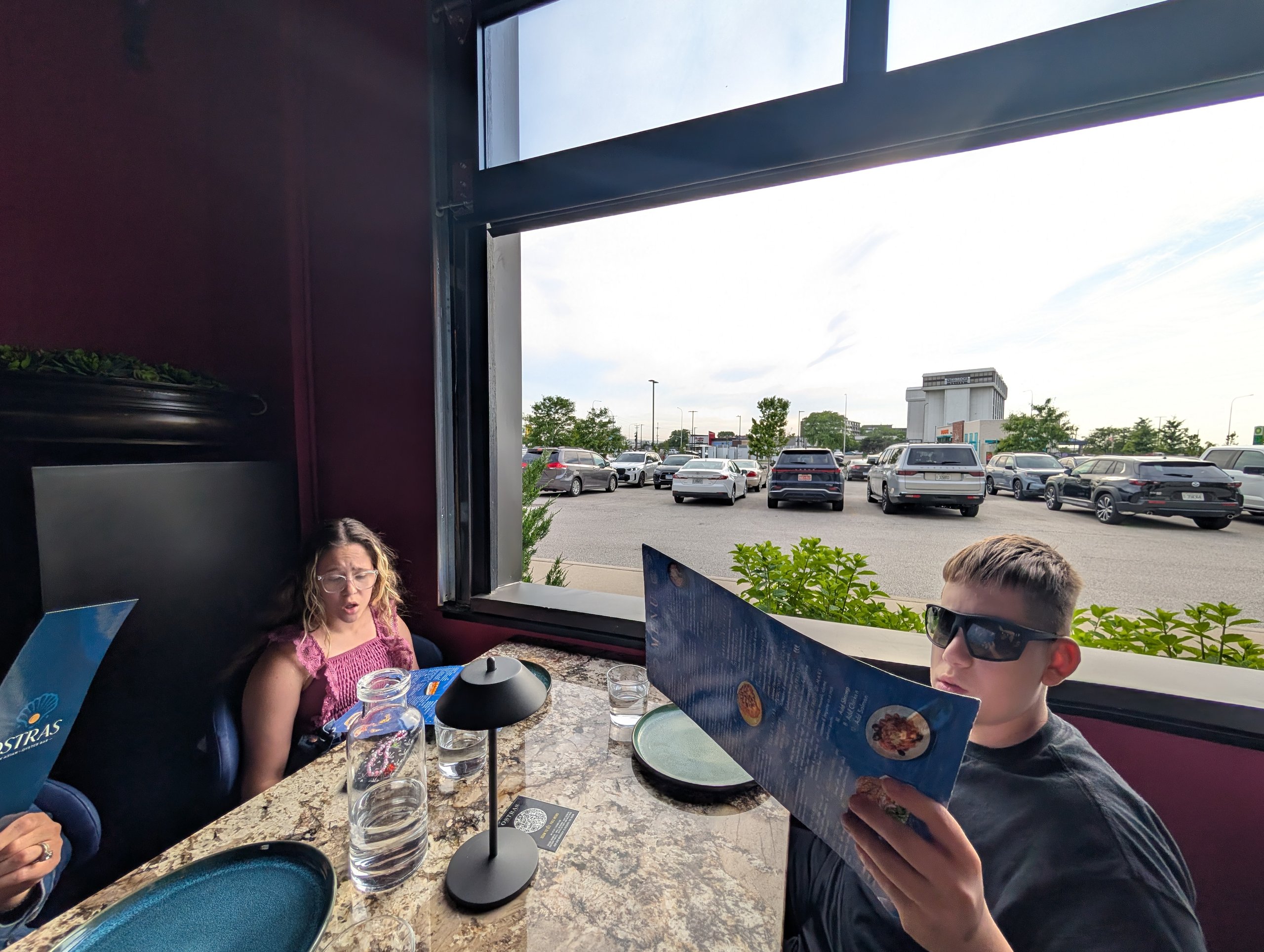 Emily and Josh reading the Ostras Lounge menu at a window booth at sunset