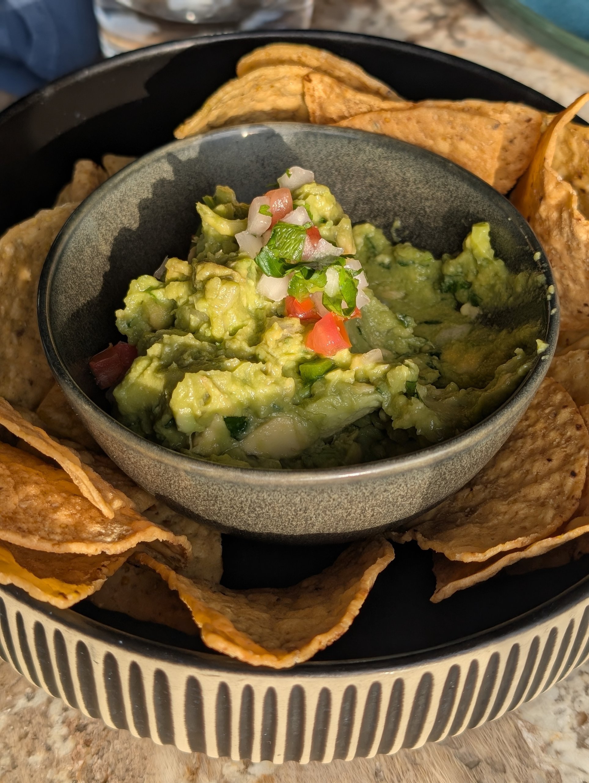 Bowl of guacamole topped with diced tomato and onion, surrounded by fried tortilla chips
