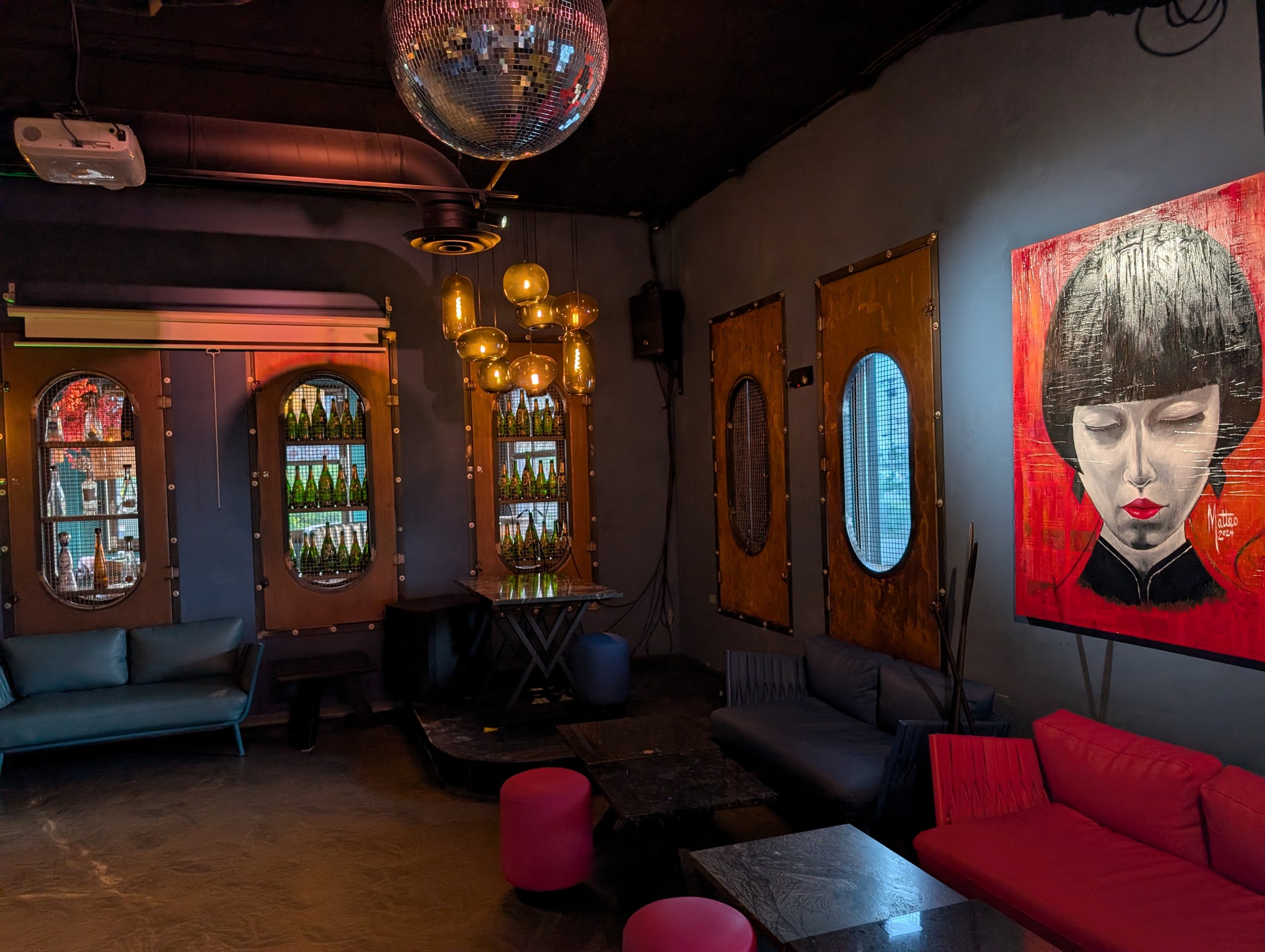 Back lounge at Ostras Lounge with a disco ball, red sofas, and large portrait paintings